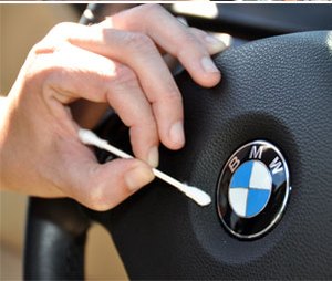 A hand using a cotton swab to clean around a car&rsquo;s steering wheel badge.